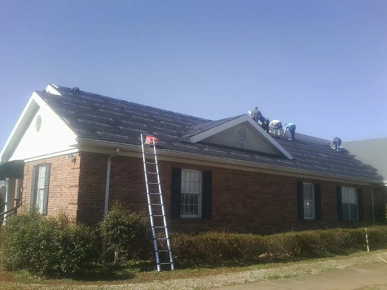 Crew tearing shingles off a brick ranch roof with a ladder set — Emergency Roof Repair work by our crew in Helotes