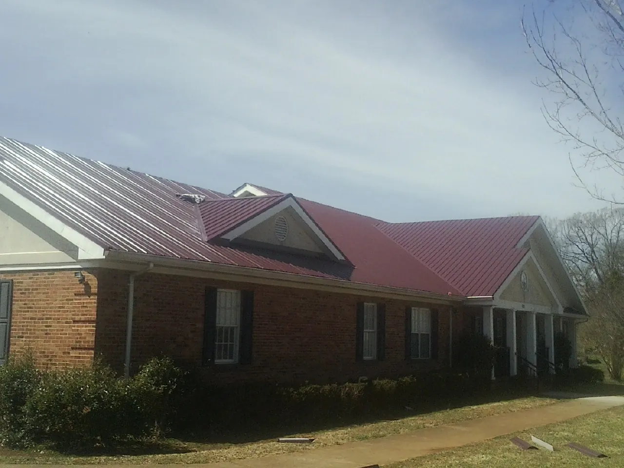 Red metal roof with gabled entries on a long brick building, from a Hail Damage Roof Repair job in Helotes