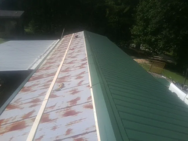 Old rusted panels beside newly installed green metal roofing — Wind Damage Roof Repair by Roofing Brothers in Helotes