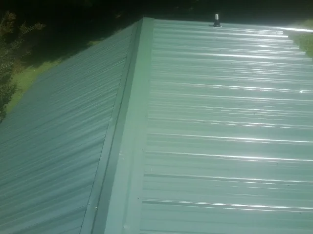 New green metal panels meeting at the ridge of a roof — Flat Roof Repair work by our crew in Helotes