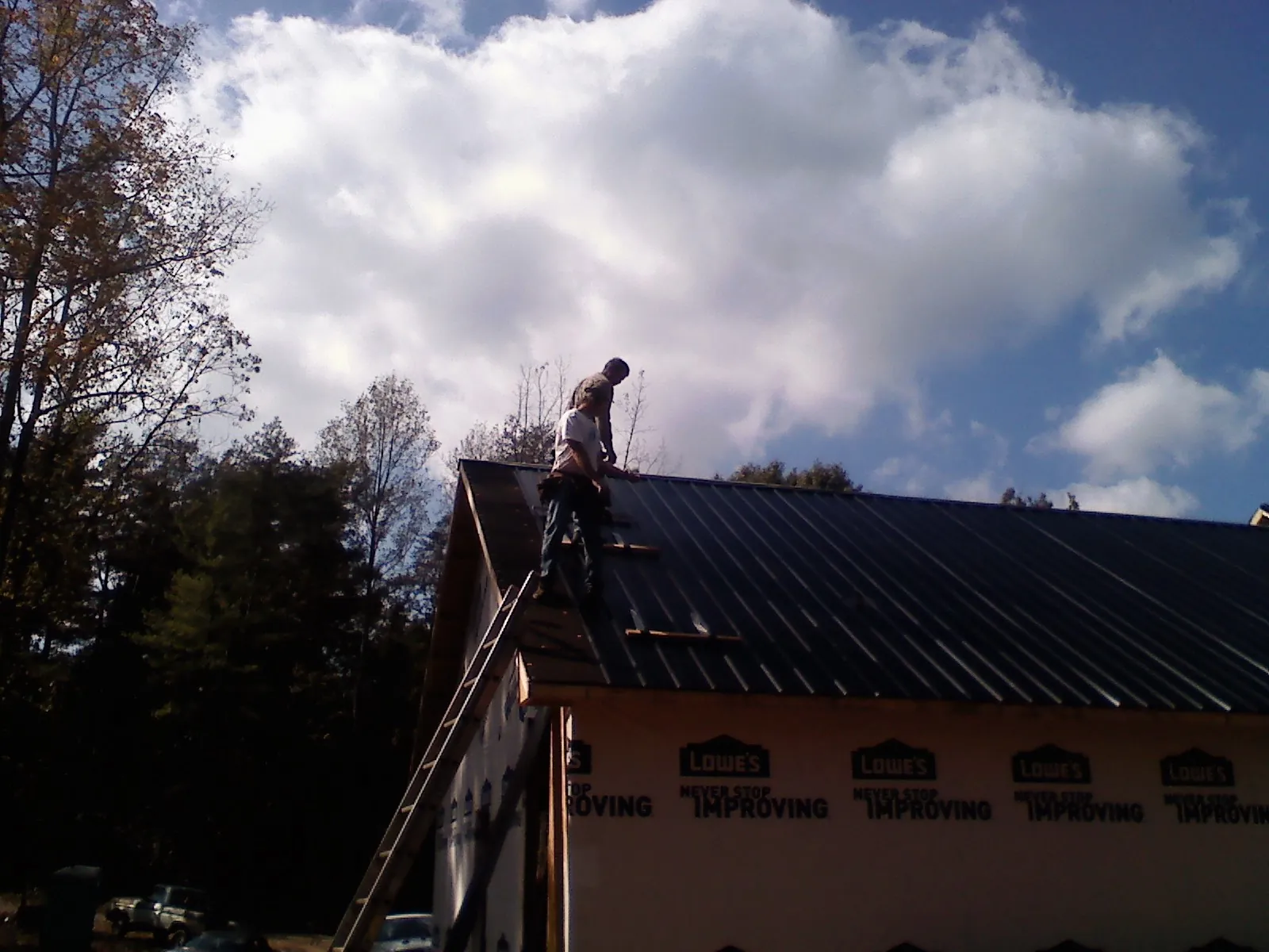 Roofer fastening dark metal panels high against a cloudy sky, from a Roof Inspection job in Helotes